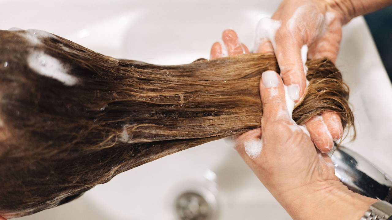 Hai bàn tay đầy bọt vuốt dọc phần tóc dài ướt trên bồn gội trắng
