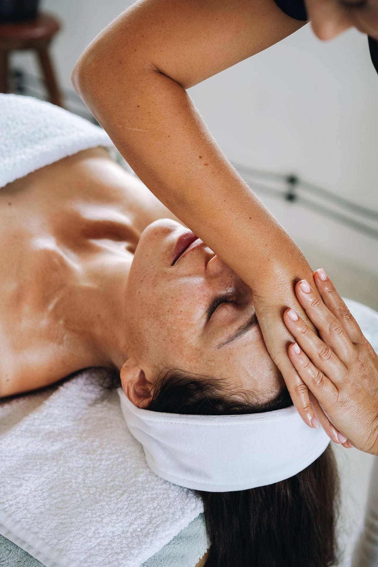 Bàn tay và cẳng tay người kỹ thuật viên đặt ngang trán và mắt một người đang nằm ngửa trên khăn bông trắng, tóc gom trong băng đô
