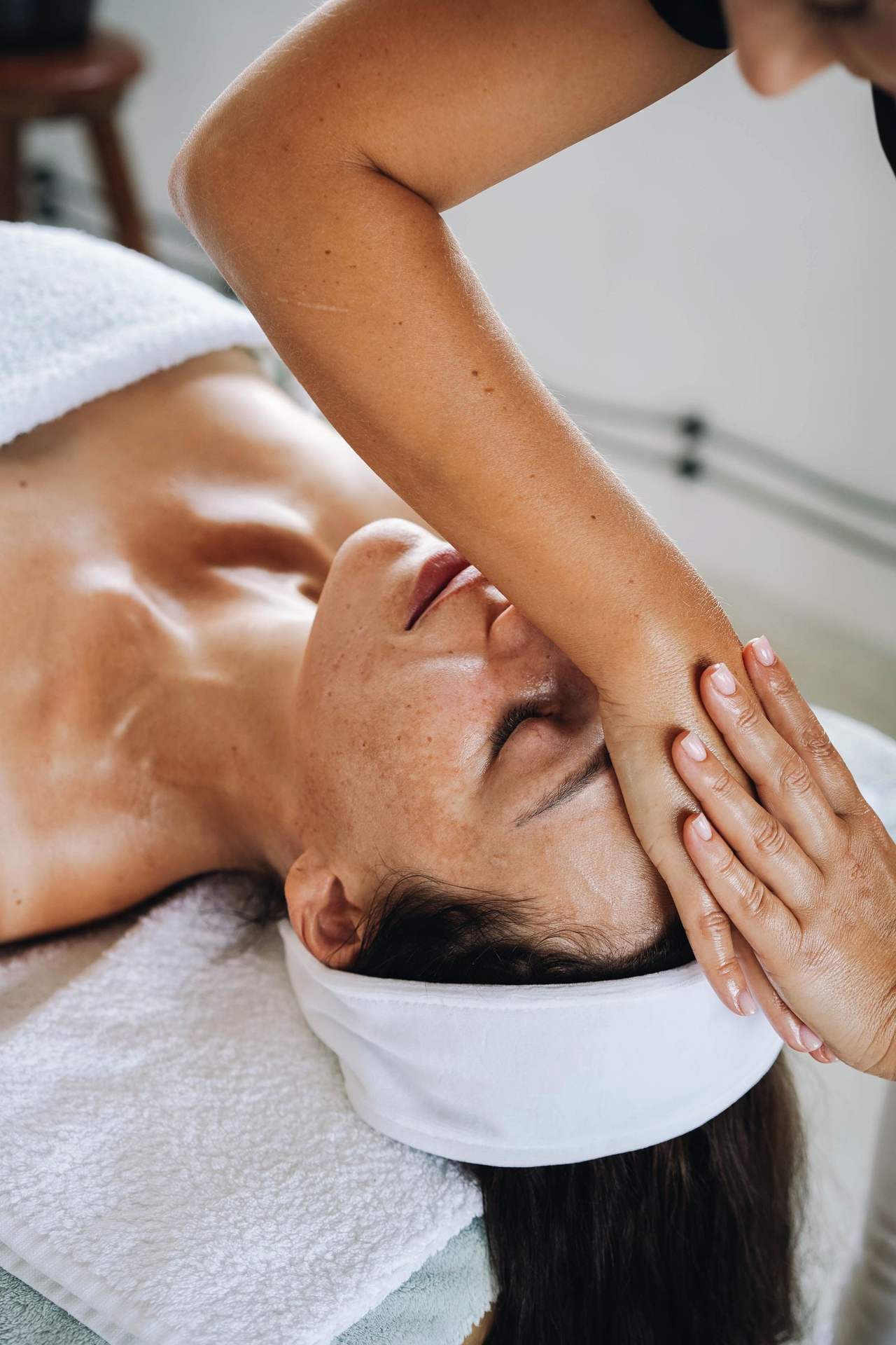 Bàn tay và cẳng tay người kỹ thuật viên đặt ngang trán và mắt một người đang nằm ngửa trên khăn bông trắng, tóc gom trong băng đô